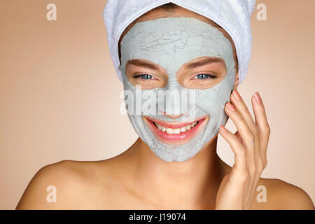 Lachende Mädchen mit Tonerde Gesichtsmaske. Glückliche junge Frau lächelnd genießen Spa-Behandlungen. Schönheit & Skin care Konzept Stockfoto