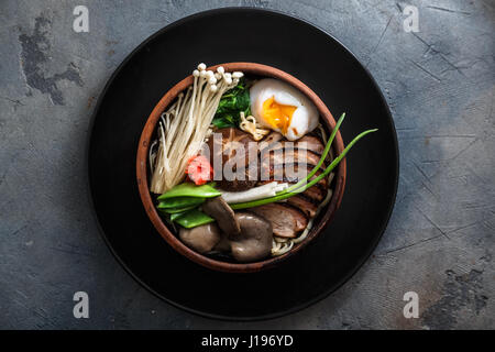 Ramen-Nudeln mit Ente, Ei, Enoki und Shiitake Pilze mit Brühe auf dunklem Hintergrund Stockfoto