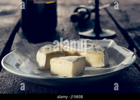 Drei in Scheiben geschnittenen Stücke von Camembert Käse auf der Platte in der Flasche Glas Wein anf Stockfoto