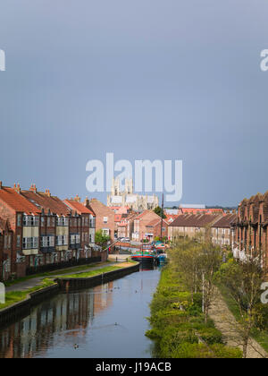 Das alte Münster im Frühjahr vom Kanal aus gesehen flankiert von Bürgerhäusern und renoviert Lastkähne auf dem Wasser in Beverley, Yorkshire, Großbritannien. Stockfoto