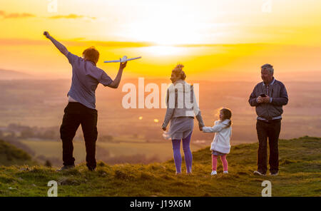 Familie auf dem Lande in den Abend im Frühjahr, wenn die Sonne untergeht, ein Spielflugzeug zu werfen und den Sonnenuntergang genießen. Zusammen Konzept. Familie bei Sonnenuntergang. Stockfoto