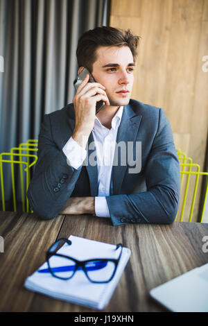 Junger Geschäftsmann in seinem Büro am Telefon Notizen - schlechte Sitzhaltung kaukasischen Stockfoto