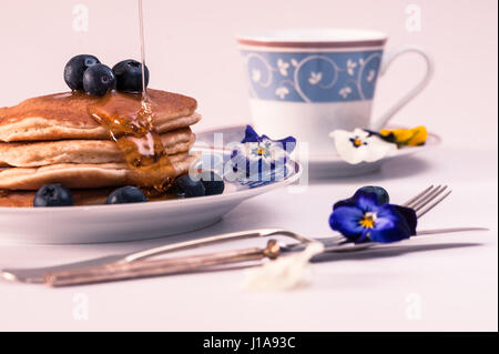 Landschaft mit blauen Blumen Tee-Set Frühstück: leckere Pfannkuchen mit Heidelbeeren und gießen Honig Sirup Stockfoto