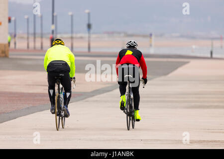 Zwei Männer zusammen Radfahren entlang der Küste direkt am Meer und Promenade von Rhyl in Nordwales während stumpf bewölktem im Sommer Stockfoto