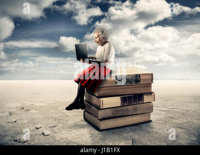 Alte Dame mit Laptop sitzen auf Bücher Stockfoto