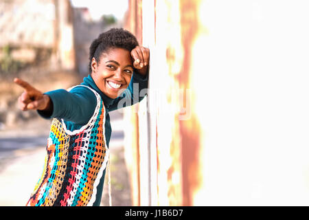 Lächelnde afroamerikanische Frau an die Wand gelehnt und Fingerzeig Stockfoto