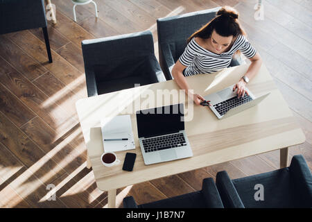 Multitasking-Frau in einem Café arbeiten auf Handy und Laptop, während ihr Kollege ruht. Stockfoto