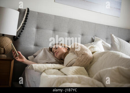 Frau im Bett SMS auf Handy Stockfoto