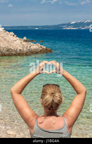 Frau gestalten ihre Hände in Herz-Symbol auf einem kleinen Kiesstrand in der Nähe von Lun, Insel Pag, Kroatien Stockfoto