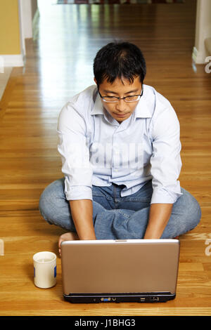 Eine asiatische Geschäftsmann, sitzen auf dem Boden auf seinem Laptop arbeiten Stockfoto