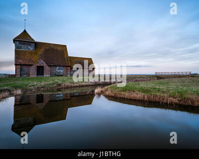 Fairfield Church, Romney Marsh, Kent, England bei Sonnenuntergang mit der Kirche in einem nahe gelegenen Deich reflektiert. Stockfoto