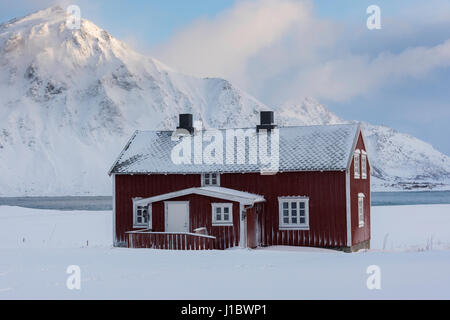 Rotes Haus im Schnee in der Nähe von Flakstad Kirche, Flakstadoya, Lofoten Inseln, Norwegen Stockfoto