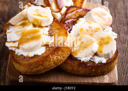 Frühstück mit hausgemachten Ricotta Toast mit Bananen in Scheiben geschnitten und Karamell-Sauce auf rustikalem Holzbrett serviert Stockfoto