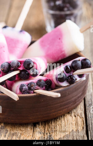 Hausgemachte Berry Joghurt Eis am Stiel dekoriert mit gefrorenen Johannisbeeren in rustikalen Keramikschale auf Holztisch Stockfoto