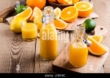Frisch gepresster Orangensaft in Flaschen vor dem Hintergrund von frischen Zitrusfrüchten Stockfoto