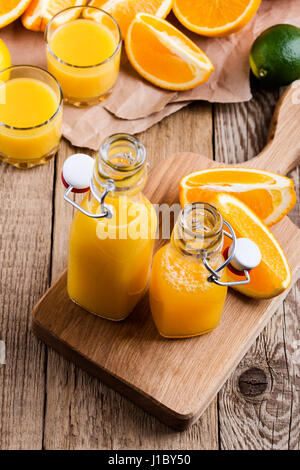Frisch gepresster Orangensaft in Flaschen vor dem Hintergrund von frischen Zitrusfrüchten Stockfoto