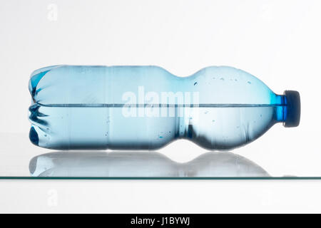 Blauen Plastikflasche Wasser auf Glasregal liegen. Halb voll oder halb leer. Stockfoto