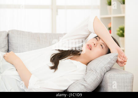 Fühlen sich gestresst. junge Frau ihren Kopf zu berühren, beim Sitzen auf dem Sofa zu Hause. Lebensstil und Gesundheit Konzept gemischt Rennen asiatische chinesische Modell. Stockfoto