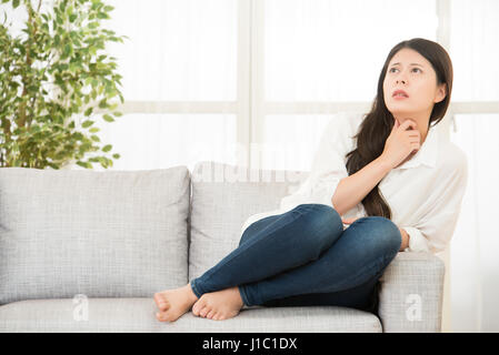 Schreckliche Schmerzen in der Kehle. junge Frau berühren den Hals beim Sitzen auf der Couch zu Hause. Lebensstil und Gesundheit-Konzept. Asiatisch Chinesisch Mischlinge Stockfoto