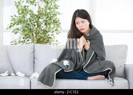 Kranke Frau gefangen kalt und Grippe. Frau Kältegefühl auf Sofa mit Decke sitzen. Medizin und Gesundheit-Konzept. asiatische chinesische Modell Mischlinge Stockfoto