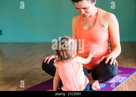 Gemischte Rennen Mädchen berühren Bauch der werdenden Mutter auf Gymnastikmatte Stockfoto