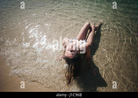 Kaukasische Frau mit Bikini in Wellen am Strand sitzen Stockfoto