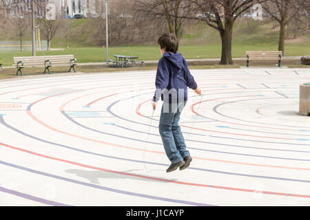 ZEHN JAHRE ALTEN SPRINGT SEIL AN WARMEN FRÜHLINGSTAG IM CHRISTIE GRUBEN PARK IN TORONTO, KANADA. Stockfoto