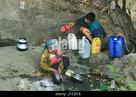 Reinigung von Töpfen und eine junge Frau Tripura sammelt Trinkwasser aus einem getrockneten Wasserfall in der Nähe von Kanglak Hügel am Sajek, Rangamati, Bangladesch. Stockfoto