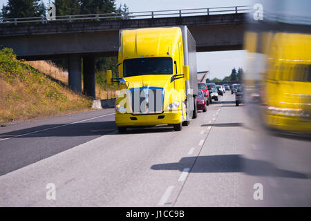 Helle moderne auffällige gelbe Lastwagen mit Anhänger mit Ladung auf der Autobahn vor den anderen Autos. LKW, fahren unter der Brücke Stockfoto