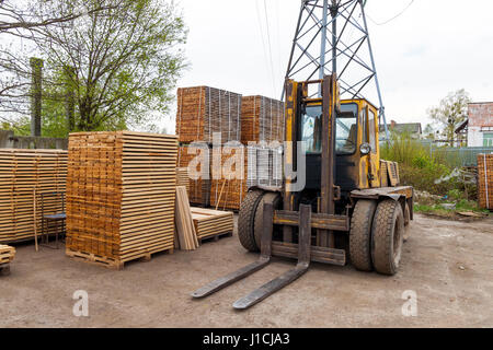 Große Gabelstapler und Stapel von neuen Holzbrettern und Nieten an den Holzplatz. Holzplatten auf Pfählen für Möbel-Materialien Stockfoto