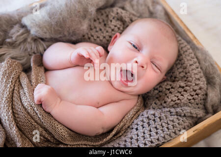 Neugeborenes Baby liegend in einer Holzkiste verpackt in gestrickte Schals und decken, Gähnen. Stockfoto