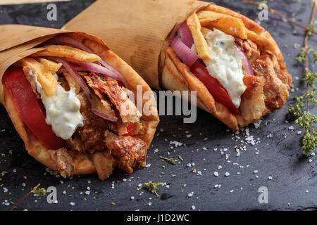 Griechische Gyros in Pita Brot auf einem schwarzen Teller gewickelt Stockfoto