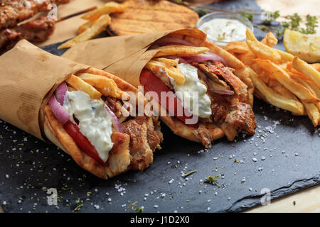 Griechische Gyros in Pita Brot auf einem schwarzen Teller gewickelt Stockfoto