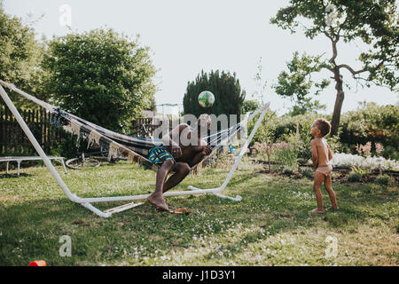 Vater in Hängematte spielt Ball mit seinem Sohn Stockfoto