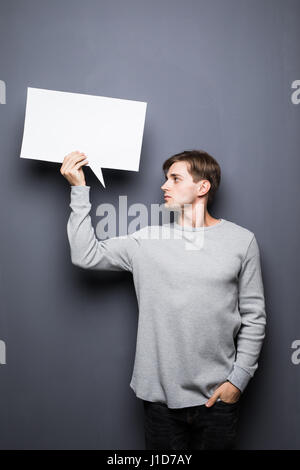Schönen jungen Mann halten weiße leere Sprechblase mit Platz für Text auf grauem Hintergrund isoliert. Stockfoto