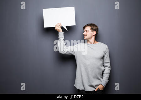 Schönen jungen Mann halten weiße leere Sprechblase mit Platz für Text auf grauem Hintergrund isoliert. Stockfoto