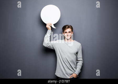 Schönen jungen Mann halten weiße leere Sprechblase mit Platz für Text auf grauem Hintergrund isoliert. Stockfoto