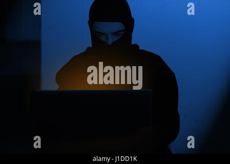 Hacker-Mann in Hoodie Shirt Eingabe hacking globale Netwok Sicherheit auf Computer Laptop über dunklen Hintergrund mit blauem Licht Stockfoto