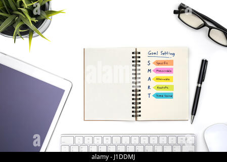 Smart-Ziel-Einstellung mit Notebook, Brillen, Stift, Maus, Tastatur, Tablet und Pflanze auf weißen Schreibtisch, Erfolgskonzept Stockfoto