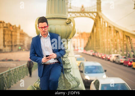 Geschäftsmann im Chat mit jemandem über das Telefon. Er steht auf einer Brücke in der Mitte einer Stadt. Stockfoto