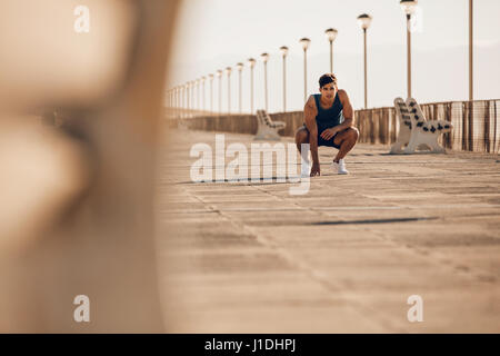 Schuss von gesunden jungen Mann eine Pause nach Morgen laufen. Männliche Läufer nach dem Ausführen auf Promenade ruhen. Stockfoto