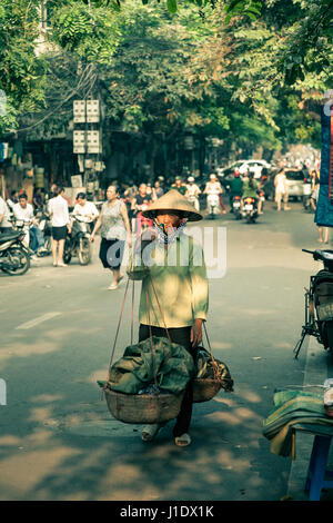 Ein vietnamesische Anbieter tragen Trachten geht durch die Straßen von Hanoi, Nordvietnam, Südost-Asien Stockfoto