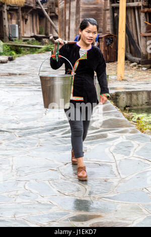 Huanggang, Guizhou, China.  Junge Frau, die Eimer auf eine Schulter Pole in einem Dong ethnische Dorf. Stockfoto