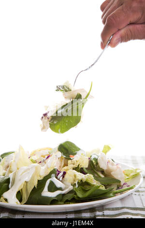 Ein Schuss von eine Hand mit einer Gabel Abholung Gemüse aus einem Teller mit Garten Salat mit dressing Stockfoto