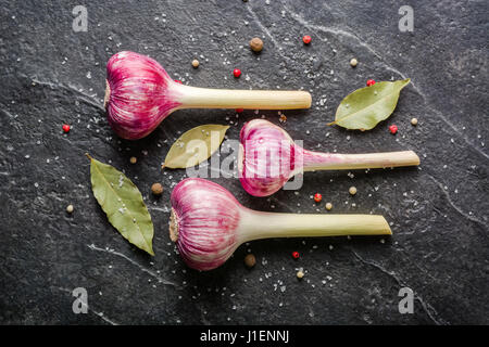 Knoblauch mit Stiel auf einem schwarzen Stein Hintergrund Lila. Eine Menge von leeren Raum. Stockfoto