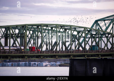 Abschnitt Struktur grün Metall Bogenbrücke mit einem Betonpfeiler und ein LKW mit einer roten Kabine und Edelstahltanks und eine Schar Vögel in den Himmel Stockfoto