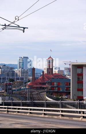 Der Bahnhof mit einem Turm und Gebäuden unter den roten Ziegeldächern und Zugang Schienen umgeben von modernen Gebäuden mit moderner Architektur Stockfoto