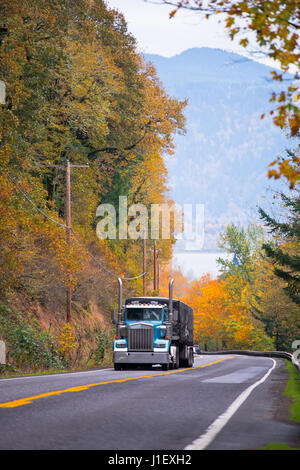 Große klassische blaue halb LKW mit Plane abgedeckt Anhänger Klettern bergauf auf einem malerischen Highway mit Metall Sicherheitsmerkmale Zaun und Straße Stockfoto