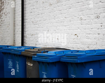 Blau und Grau Kunststoff Entsorgung / Mülleimer gegen eine gemalte weiße Mauer außerhalb eines Hauses im Royal Borough of Windsor and Maidenhead, Großbritannien Stockfoto