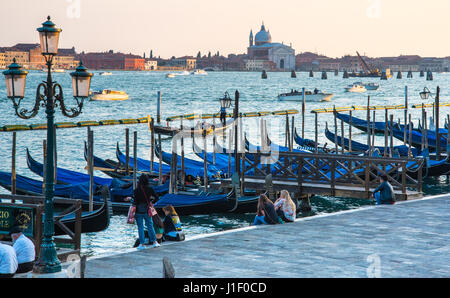 Touristen sitzen am Ufer des Riva Degi Schiavoni promenade mit Blick auf St. Marks Becken, Venedig Stockfoto